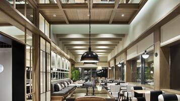 Un interior moderno con un suelo de baldosas blanco y negro geométricas, vigas de madera en el techo y una zona de estar central con mesas y sillas.