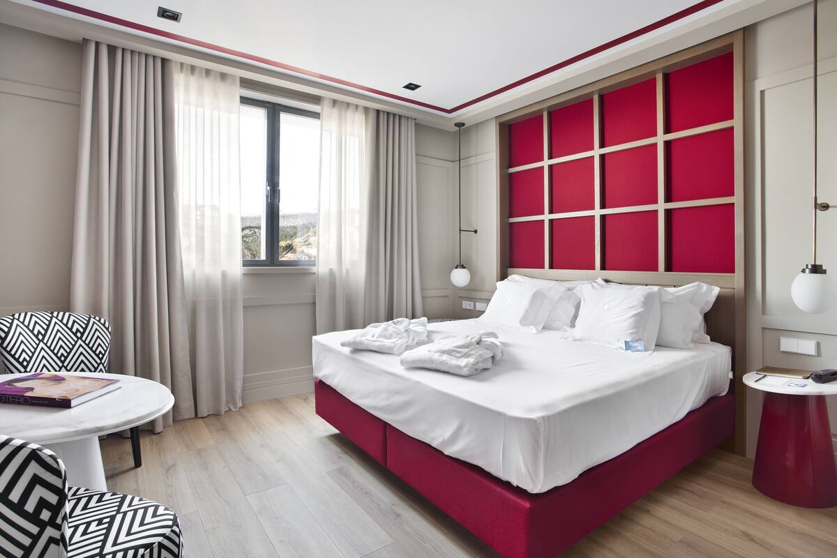 Een hotelkamer met een bed, een ronde tafel, een stoel en een raam met gordijnen.
