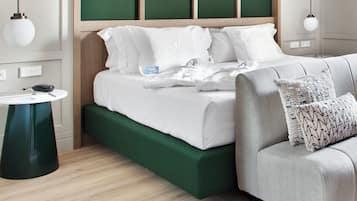 A neatly made bed with white linens, a green upholstered bench, and a round table with a black object on it.