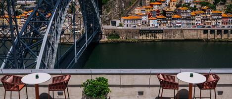 A terrace with wicker furniture and a view of a bridge and buildings.
