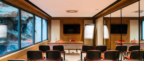 A conference room with a long table, multiple chairs, a large window, and a flat-screen TV.