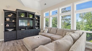A living room with a sectional sofa, dark entertainment unit, and large windows. - It's All Good In Corolla: Soundside, Pool, Spa (Corolla)