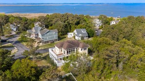 An aerial view of a residential area with houses surrounded by dense trees, a beach in the background, and a clear sky. - It's All Good In Corolla: Soundside, Pool, Spa (Corolla)