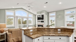 Una cocina amplia con encimera de granito, armarios blancos y ventanas grandes con vistas al exterior.