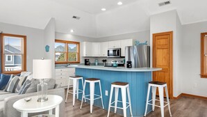 Une cuisine moderne avec des meubles blancs, un îlot central doté de tabourets et un réfrigérateur.