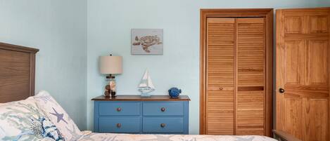 A bedroom with a bed, a dresser, a nightstand, a lamp, and a wooden wardrobe.