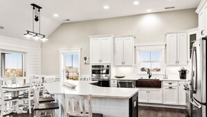 Cocina moderna con muebles blancos, una isla central con taburetes, electrodomésticos de acero inoxidable y vistas a la ciudad.