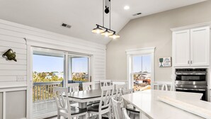 Una cocina moderna con armarios blancos, una isla grande y una zona de comedor con sillas blancas.