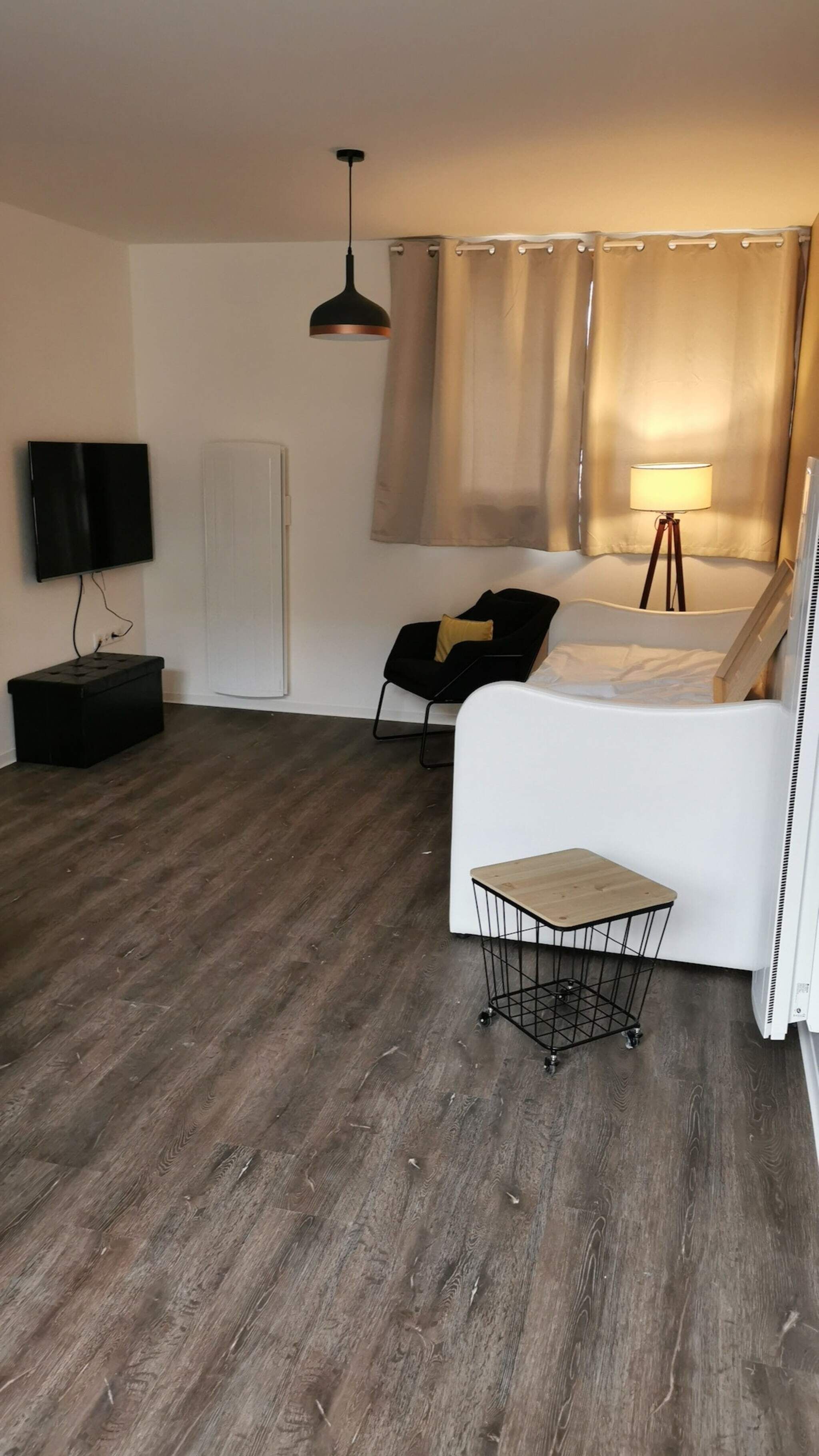 Un soggiorno moderno con una TV a schermo piatto, un poggiapiedi nero, un divano bianco, un piccolo tavolino e una lampada da terra.