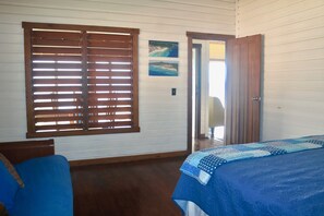 A room with a bed, a blue sofa, wooden blinds, and a door leading to another room.