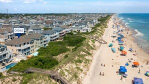 Eine Küstenwohngegend mit Häusern direkt am Strand, ein Sandstrand mit Sonnenschirmen und freier Sicht auf den Ozean.