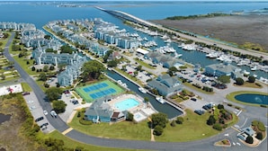Luchtbeeld van een kustwoongebied met meerdere appartementencomplexen, een jachthaven met boten en een groot zwembad.