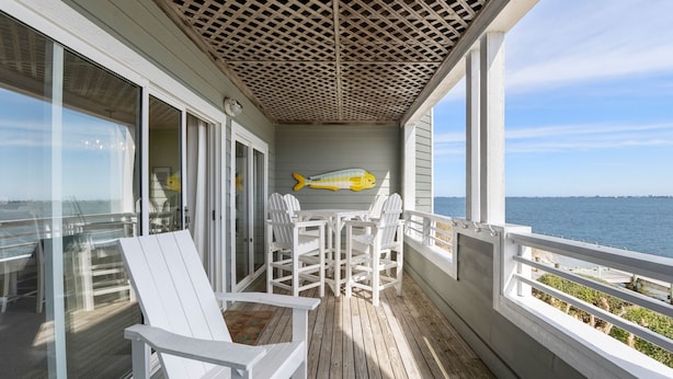 Een overdekt terras met een tafel en stoelen, een muurschildering van vissen en uitzicht op zee.