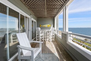 A covered deck with a table and chairs, a fish mural, and a view of the sea. - Pearl Of The Sound: Sound Views, Shared Pool (Manteo)