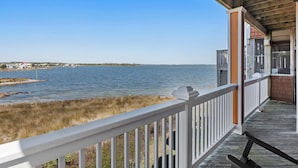 A wooden deck with a railing overlooking a body of water and a distant shoreline. - North Bay Retreat: Waterfront, Shared Pool, Fitness Center, Short Stays Anytime (Manteo)