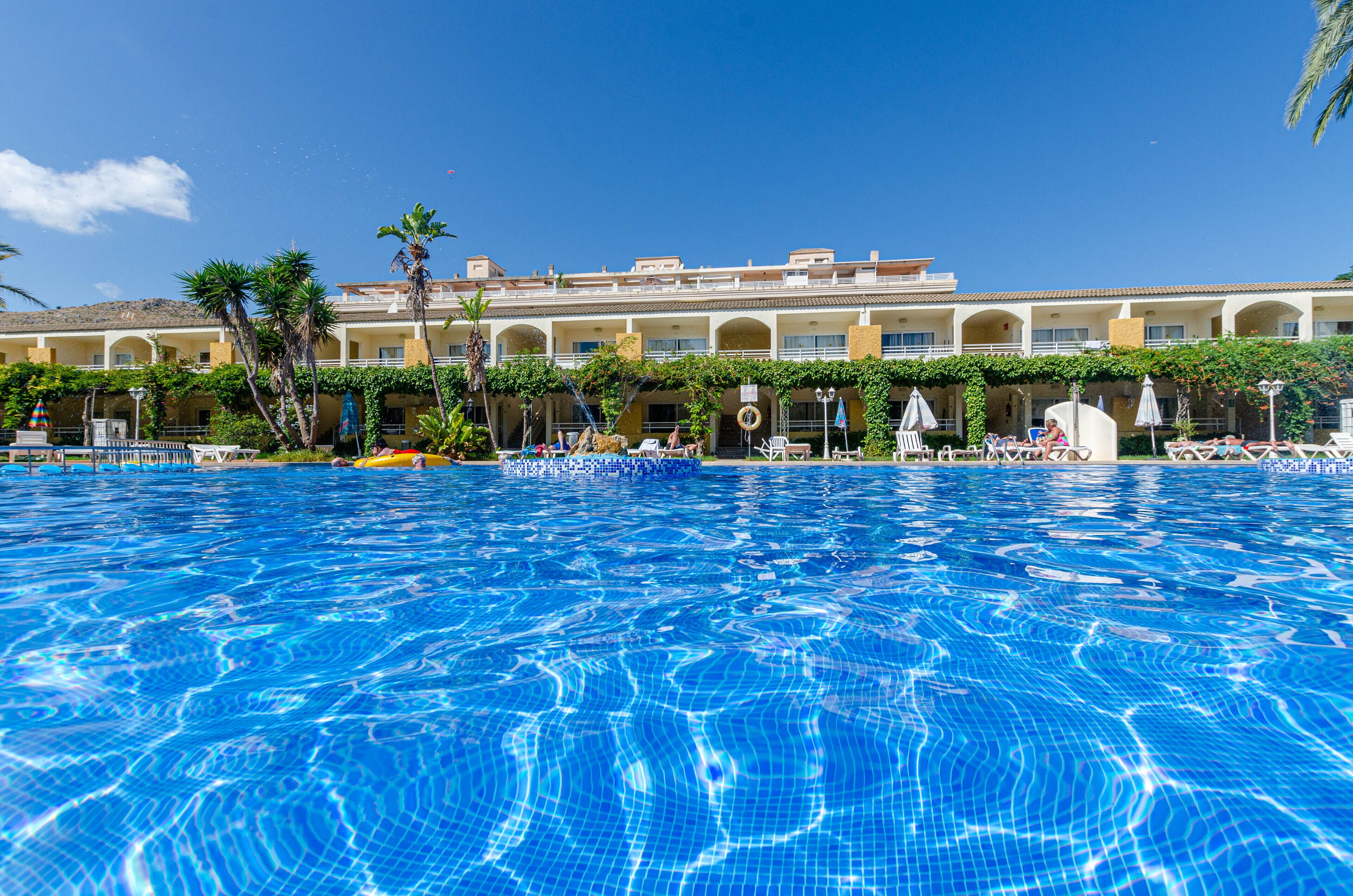 Une piscine à l’eau d’un bleu cristallin, entourée d’un bâtiment doté de nombreux balcons et bordée de palmiers.