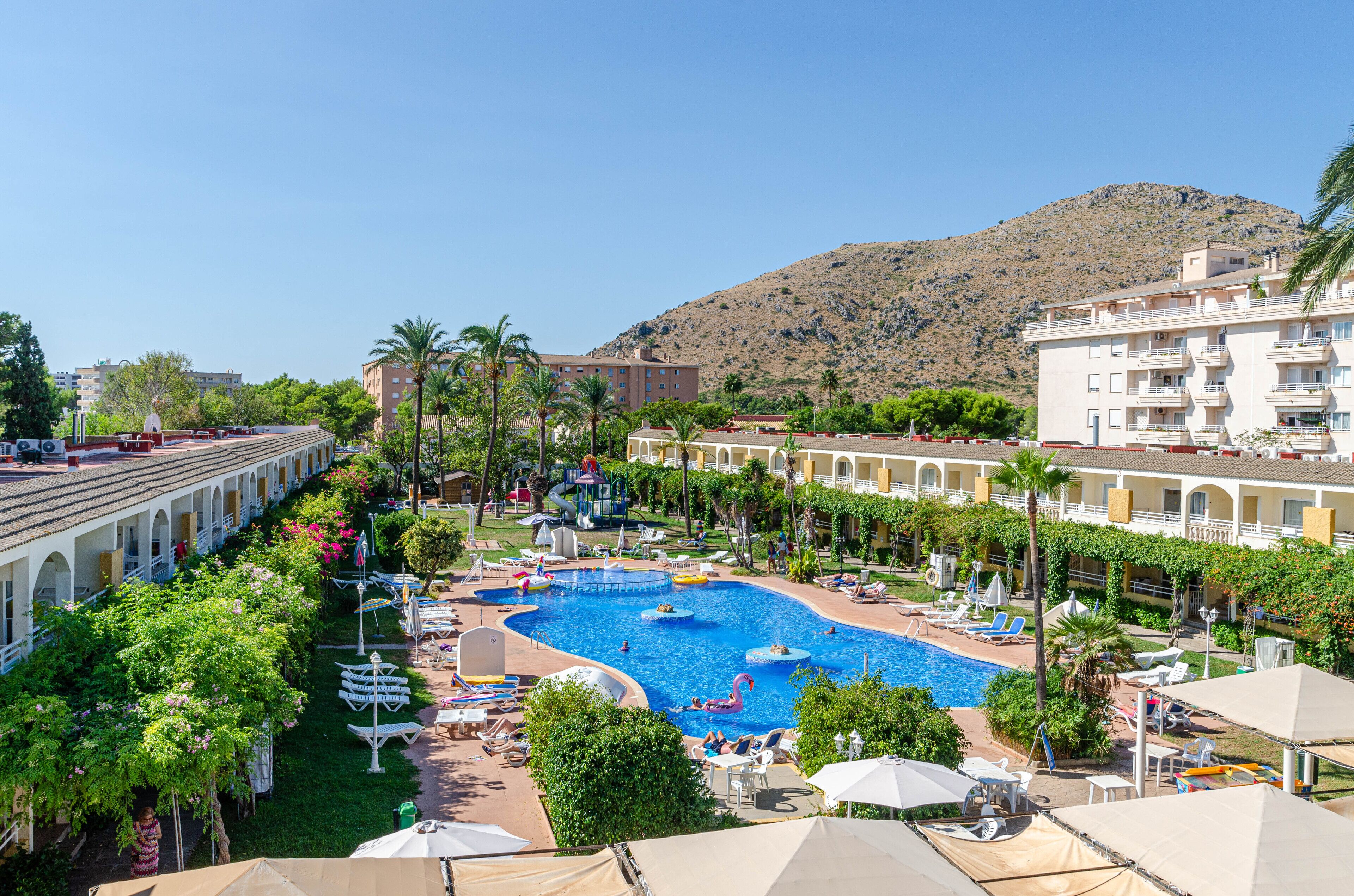 A resort with a central swimming pool, multiple lounge areas, and a mountainous backdrop.