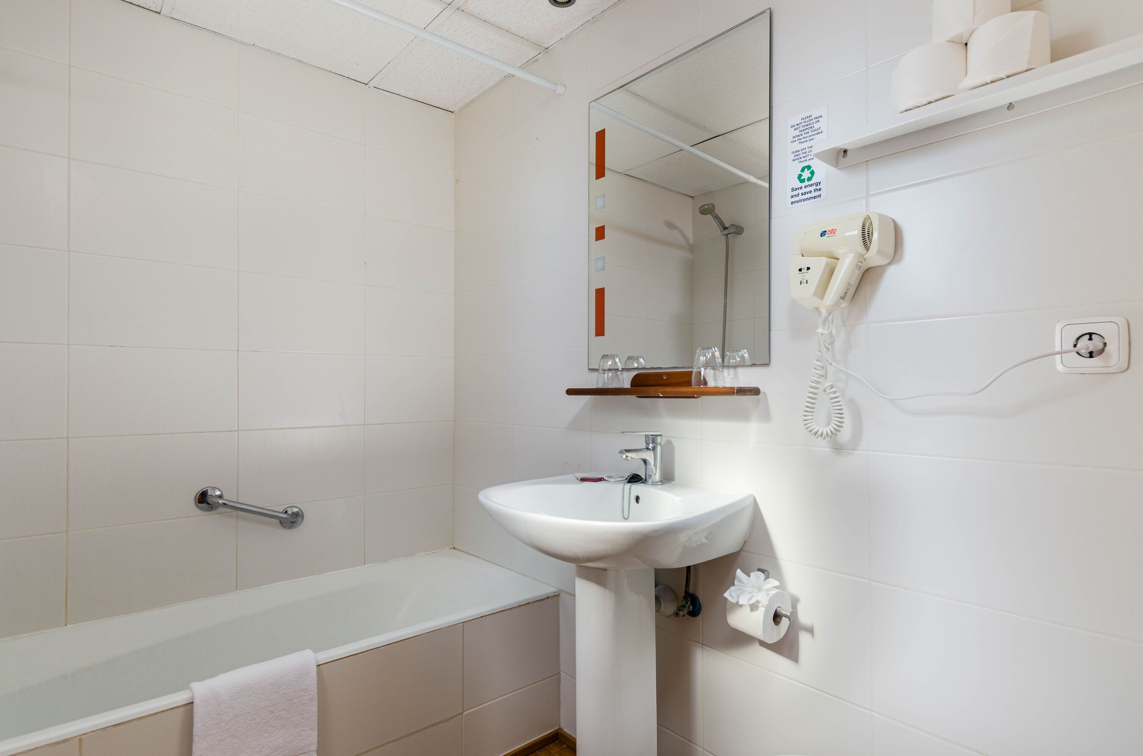 A bathroom with a bathtub, a sink, a mirror, a towel rack, and a shelf with toiletries.