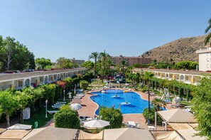 A hotel with a central swimming pool, outdoor seating, and a mountainous backdrop. - Mariner Club Apartments (Alcúdia)