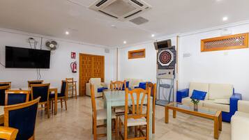 A hotel lobby with a dining area, sofas, a TV, and a dartboard.