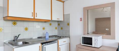 Una cucina compatta con mobili bianchi, un forno a microonde e un lavandino.