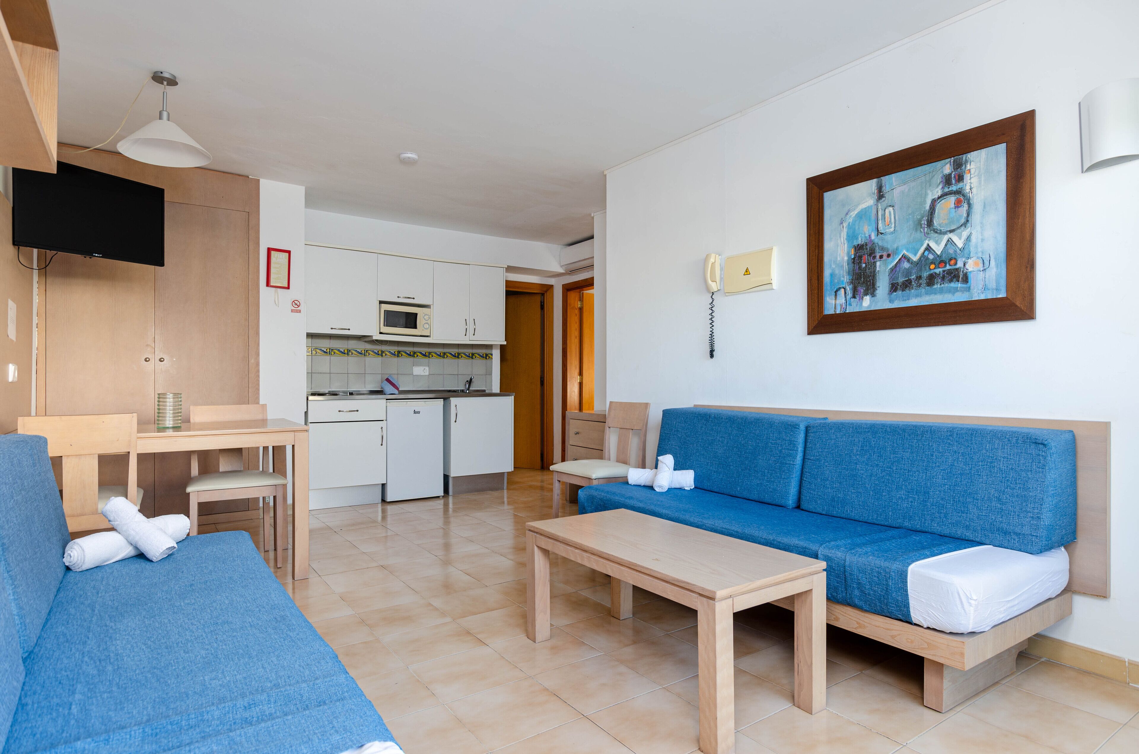 A modern living room with a blue sofa, a wooden coffee table, and a TV mounted on the wall.