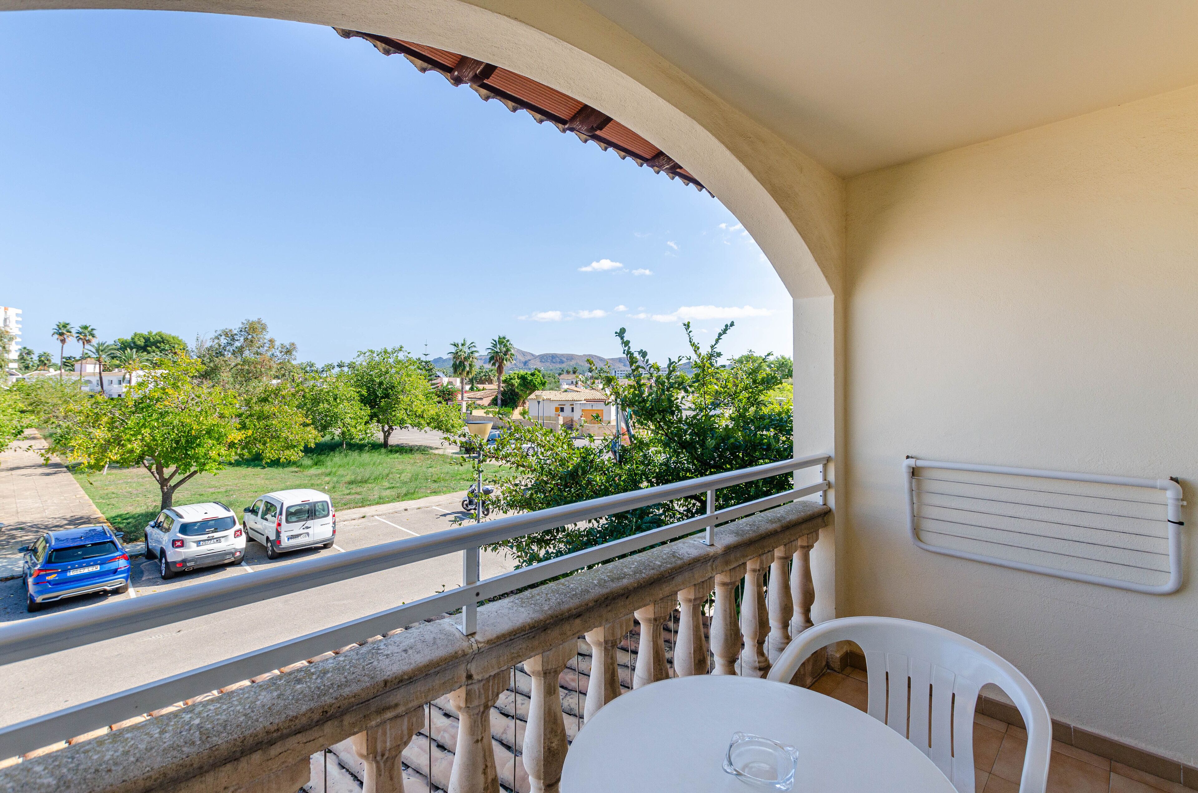 A balcony with a view of a road, parked cars, and greenery.