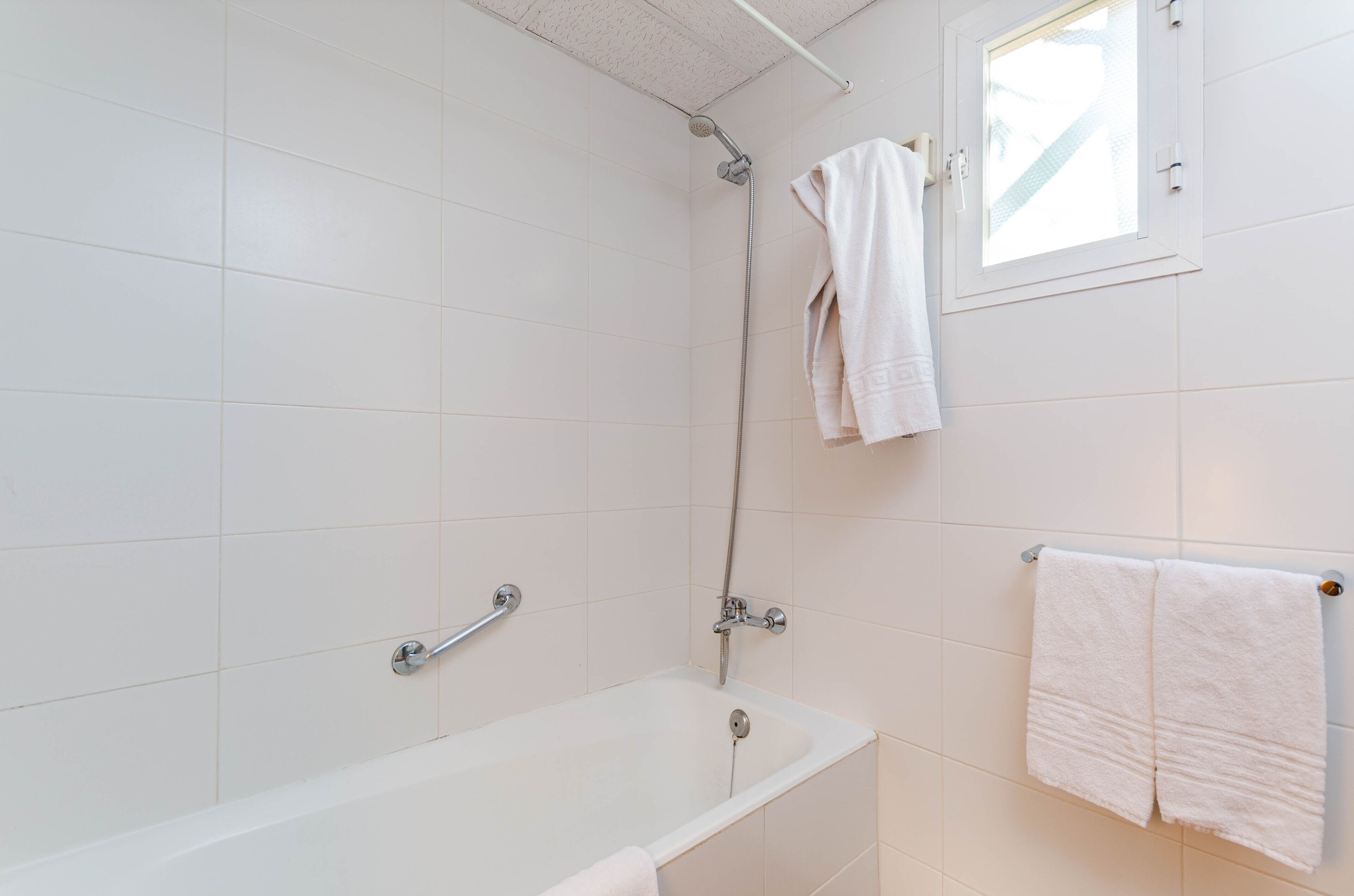 Un baño con azulejos blancos, una bañera, una ducha y dos toallas colgadas en ganchos.