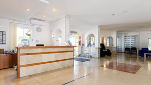 A hotel reception area with a reception desk, a waiting area with chairs, and a visible fire extinguisher. - Mariner Club Apartments (Alcúdia)