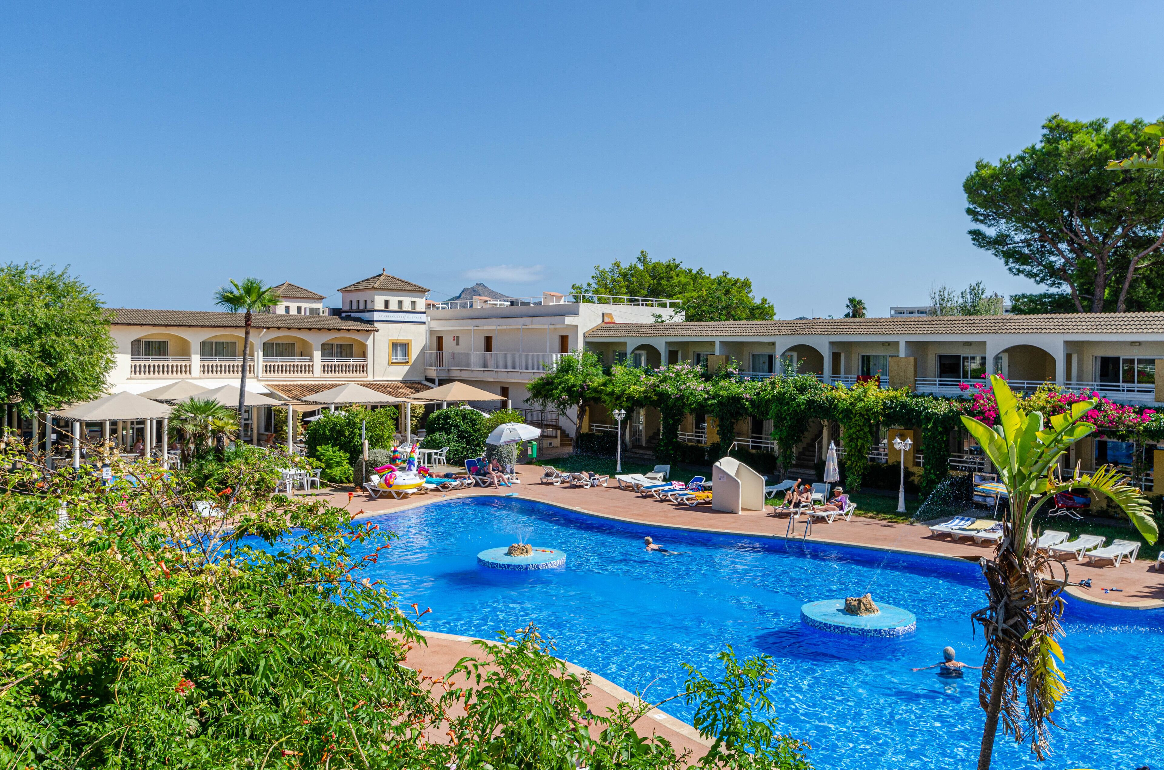A resort with a large swimming pool, sun loungers, and a covered patio area.