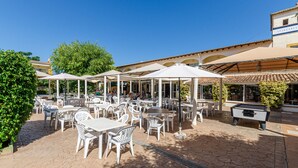 An outdoor patio area with white tables and chairs, umbrellas, and a pool table. - Mariner Club Apartments (Alcúdia)