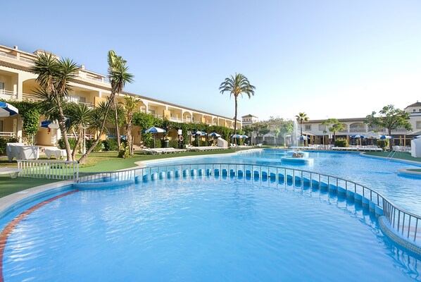 A swimming pool with a curved design, surrounded by palm trees and lounge chairs. - Mariner Club Apartments (Alcúdia)