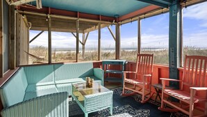 A covered outdoor seating area with wicker furniture and rocking chairs, overlooking a natural landscape.