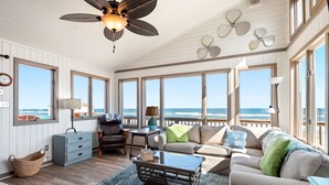 A spacious room with a large window overlooking the ocean, a ceiling fan, and a cozy seating area with a coffee table.