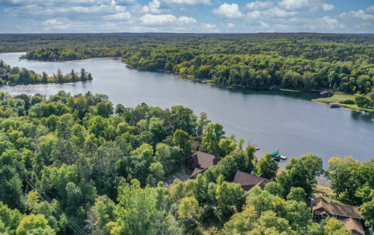 A lake surrounded by dense forest and houses with visible roofs.