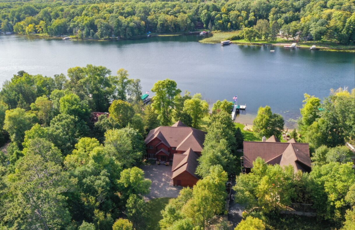 A lakeside property with two main buildings surrounded by dense trees.