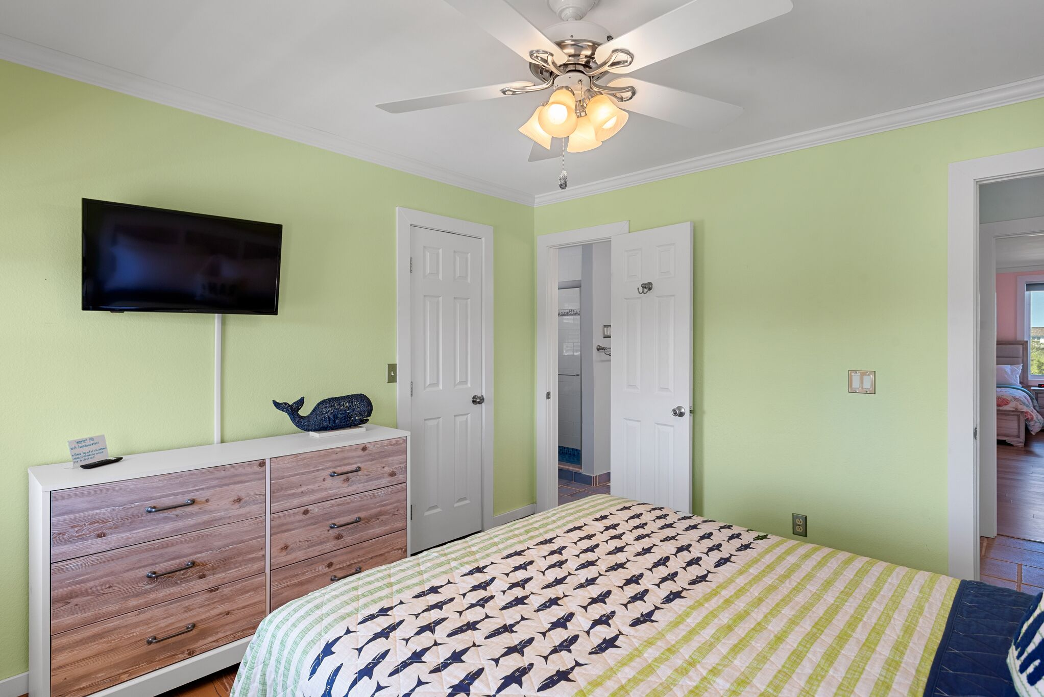 A bedroom with a bed, a dresser, a television, and a ceiling fan.