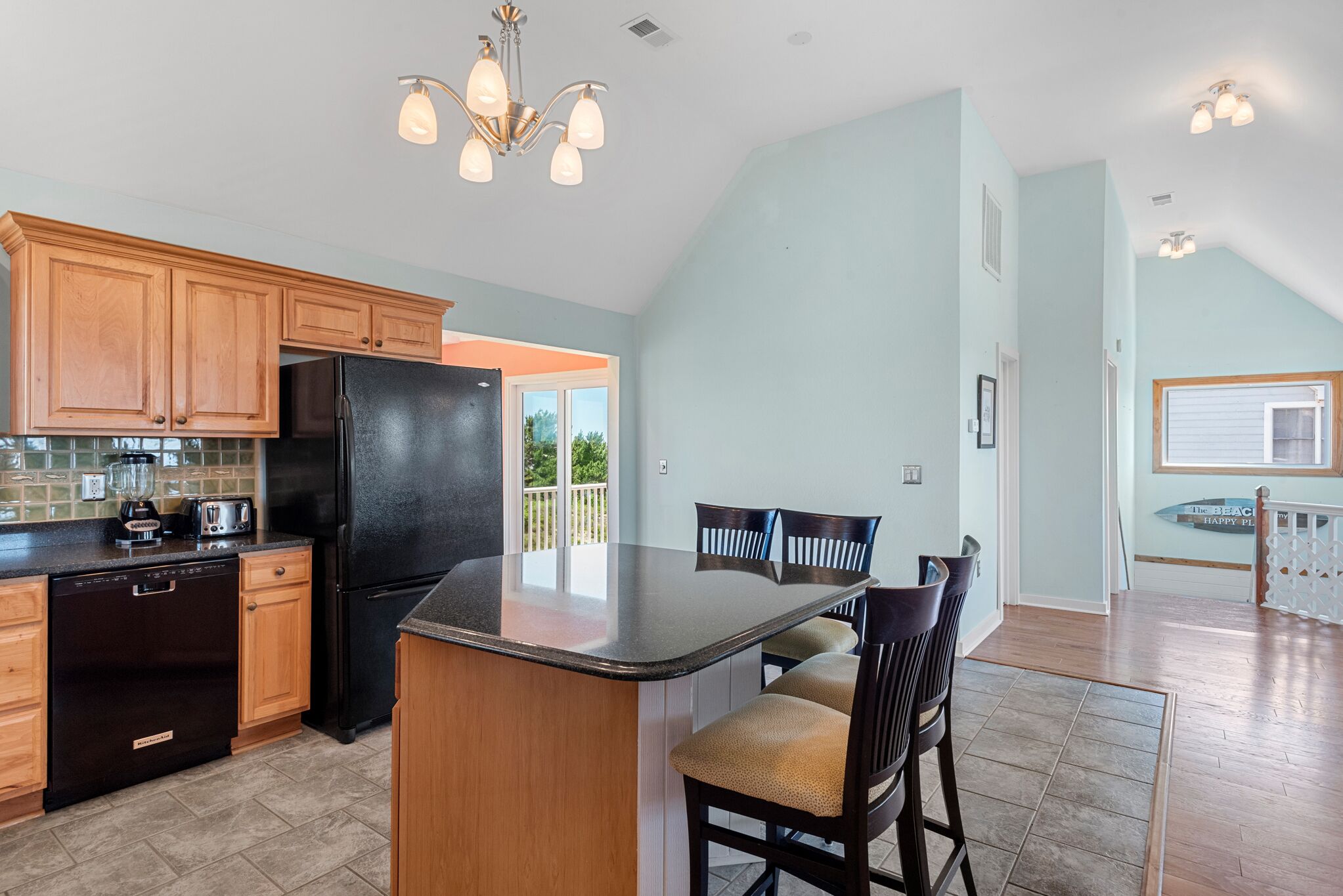 A kitchen with wooden cabinets, a black refrigerator, a built-in island, and a dining area with chairs.
