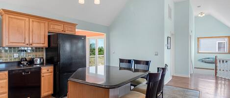 A kitchen with wooden cabinets, a black refrigerator, a built-in island, and a dining area with chairs.
