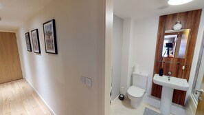 A hallway with framed pictures on the wall, a wooden door, and a white toilet with a wooden vanity and sink. - Central Perks Apartment (Hull)
