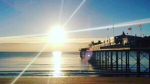 A pier extending into calm waters with the sun low on the horizon, creating a bright glare. - City Heart Brighton (Brighton)