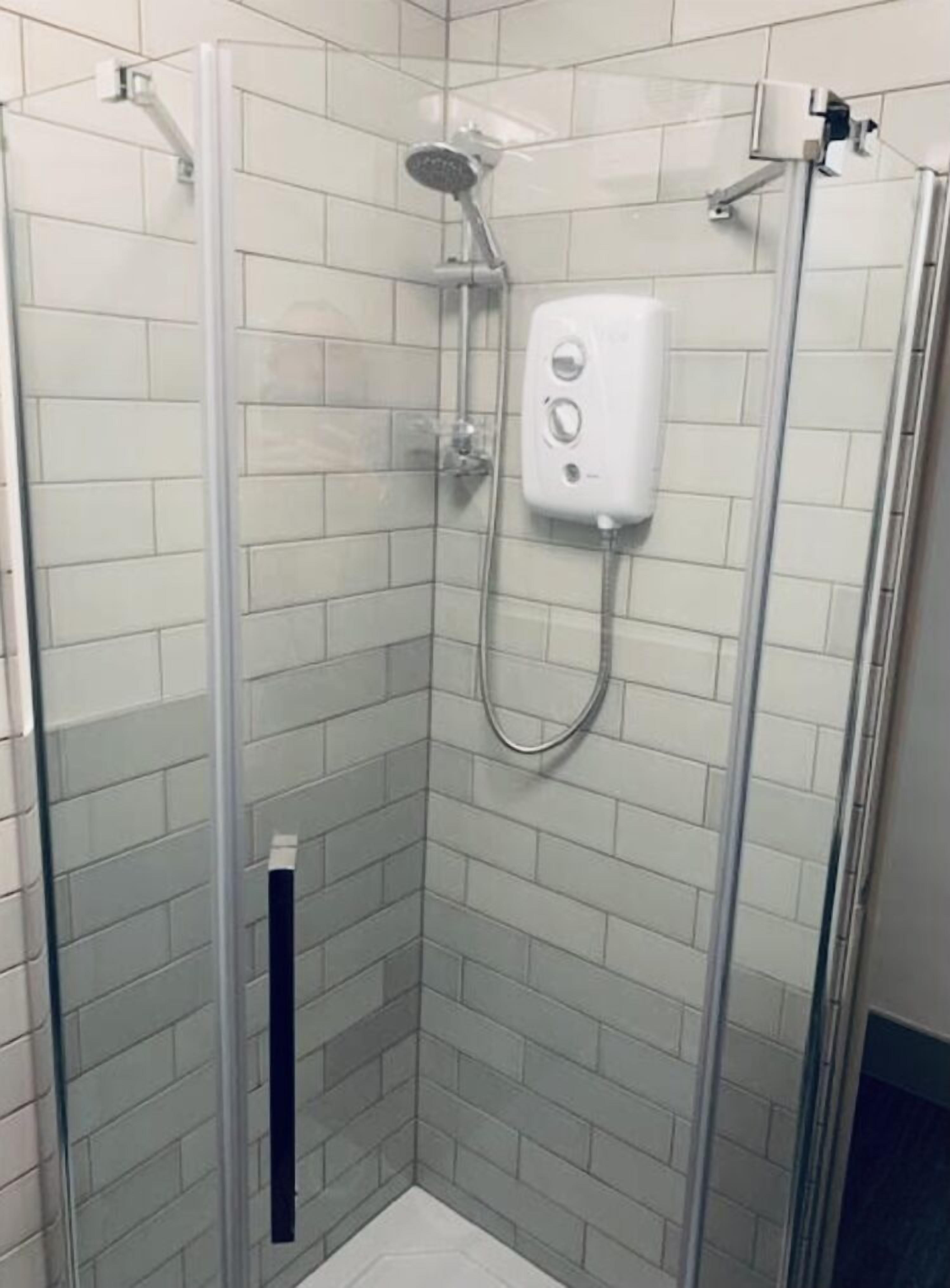 A glass-enclosed shower stall with a handheld showerhead and a wall-mounted control panel.