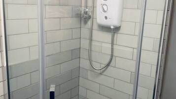 A glass-enclosed shower stall with a handheld showerhead and a wall-mounted control panel.