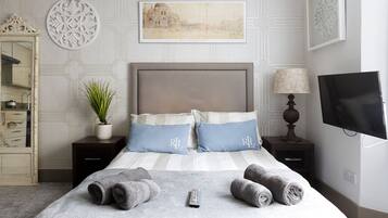 A neatly arranged bedroom with a bed, bedside tables, a lamp, a TV, and a decorative wall piece.