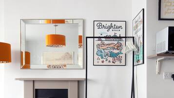 Una habitación moderna con chimenea, una mesa redonda y dos sillas. Hay cuadros en la pared, incluyendo uno que dice 'Brighton Beach'.