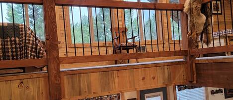 Une cabane spacieuse avec une mezzanine, de grandes fenêtres et un salon confortable doté d’un canapé et d’une cheminée.