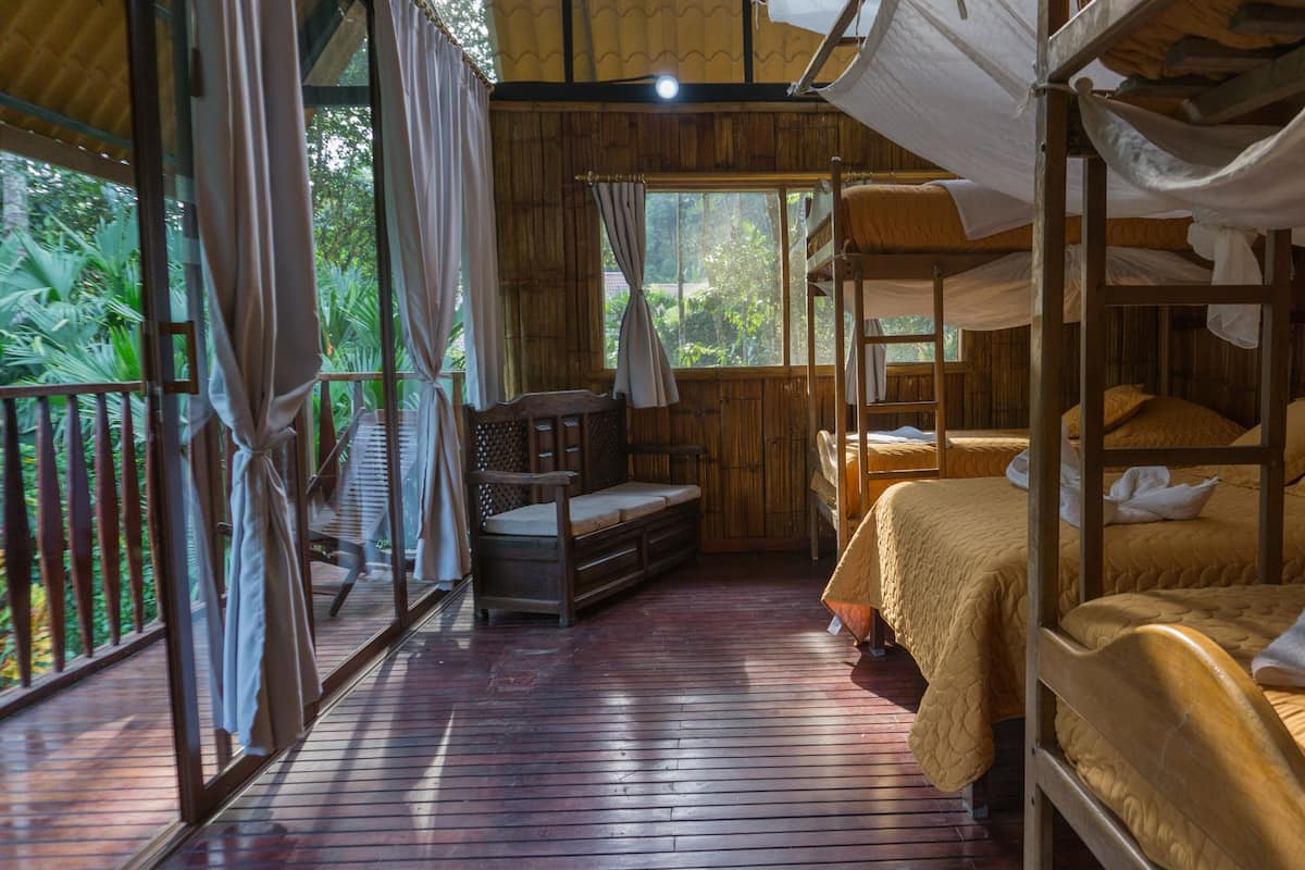 Una cabaña de madera con literas, un banco de madera y un balcón con cortinas.