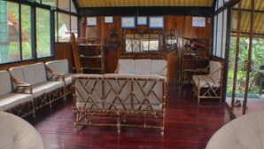 Una habitación con suelo de madera, muebles de mimbre y ventanas amplias.