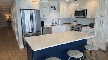 A modern kitchen with white cabinets, stainless steel appliances, a marble island, and bar stools.
