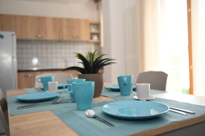 Una mesa de comedor dispuesta con platos, tazas y cubiertos azules, una planta en maceta y una ventana con cortinas.